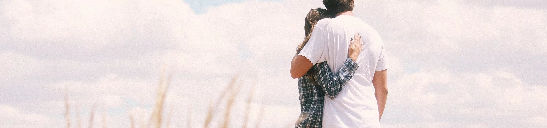A couple stands together in a lush field of tall grass, enjoying a serene moment in nature.