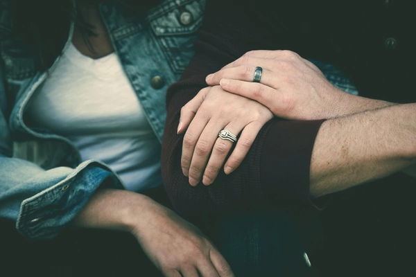 A couple holding hands, showcasing their wedding rings, symbolizing their commitment and love for each other. A couple holding hands, showcasing their wedding rings, symbolizing their commitment and love for each other.