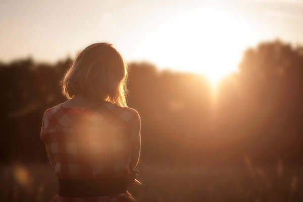 A woman stands in a field, silhouetted against a vibrant sunset sky. A woman stands in a field, silhouetted against a vibrant sunset sky.