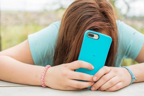 A girl holds her phone to her face, appearing engaged in a conversation or viewing content on the screen.